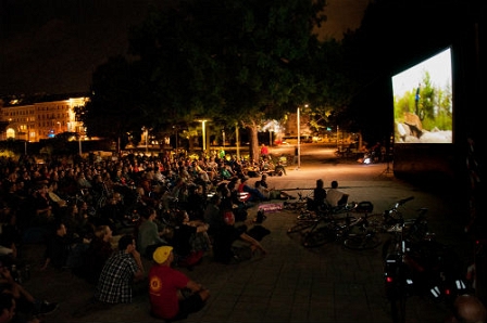 Menschen sitzen vor einer Leinwand am Boden und schauen Filme